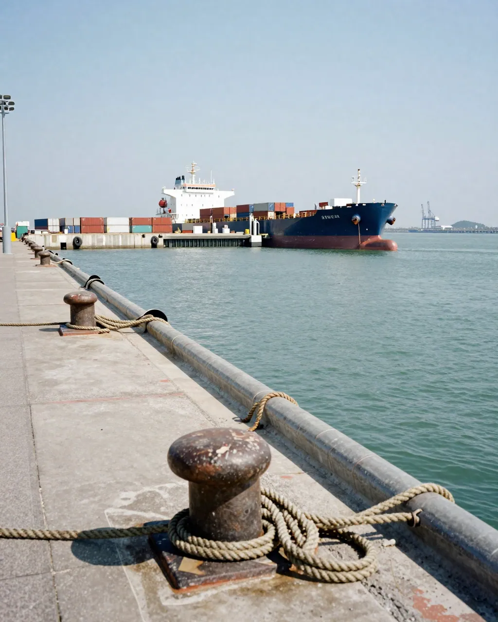A moored tanker and pipelines at a coastal terminal under hazy midday light.