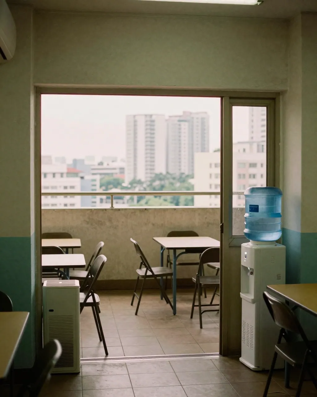 A quiet community room with chairs and an air purifier, hazy high-rises visible through the open door.