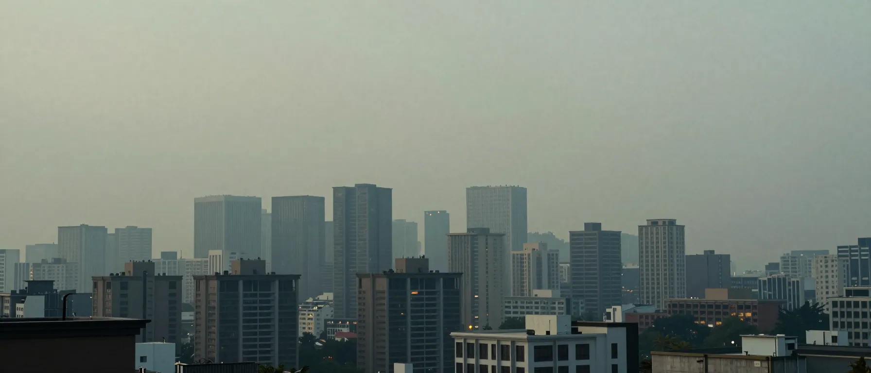 A hazy city skyline seen from a rooftop, high-rises fading into grey layers.
