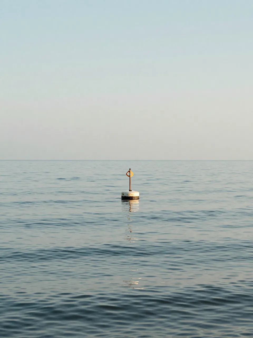 A calm sea at midday with gentle ripples and a single bobbing buoy.
