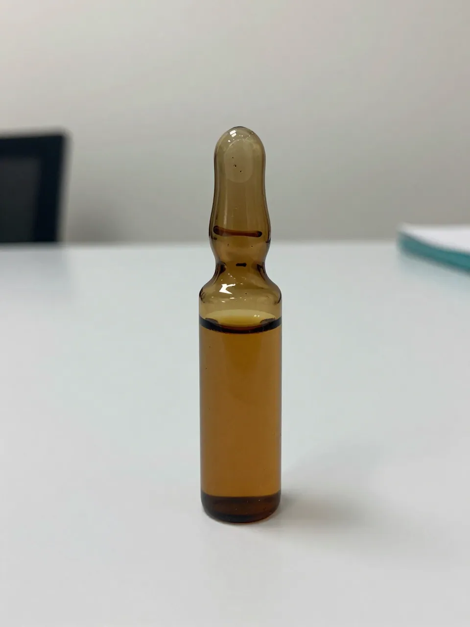 Single unlabeled amber vial with clear cap on a white lab surface.