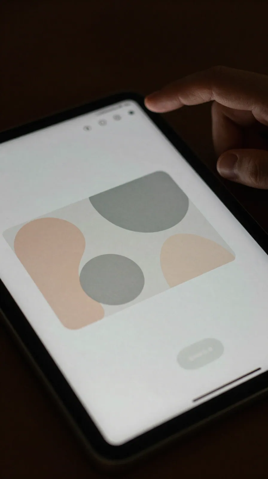 Angled close-up of a tablet screen showing an abstract ad panel with blurred button, dim room light.
