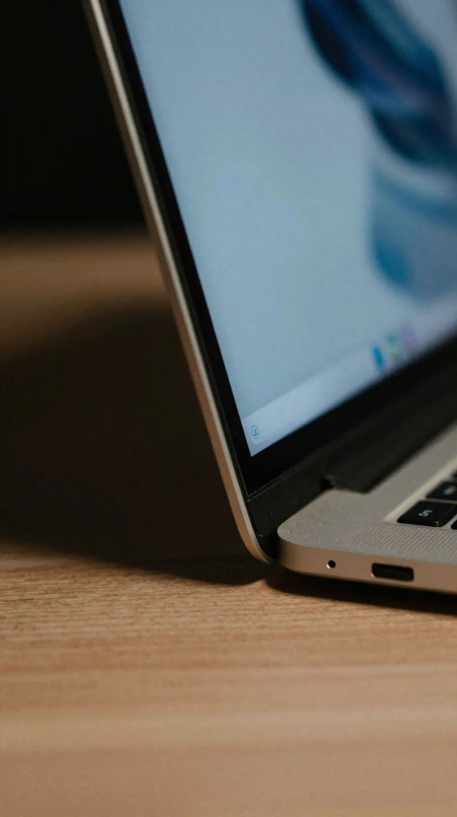 Macro view of a laptop screen edge and hinge with a crack-like reflection, dark room, blurred interface.