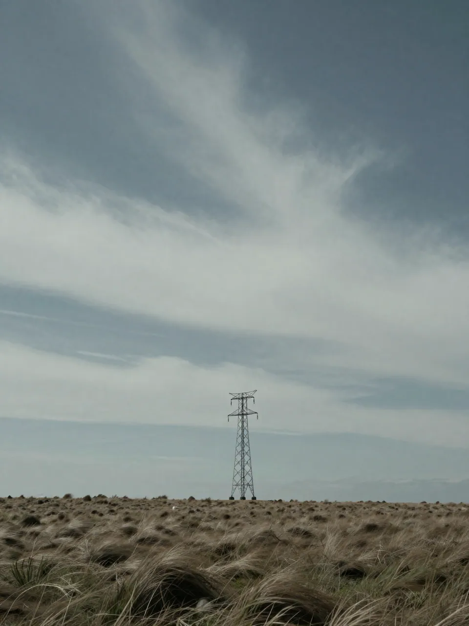 Lone transmission tower on a windswept coastal ridge under a streaked storm sky.