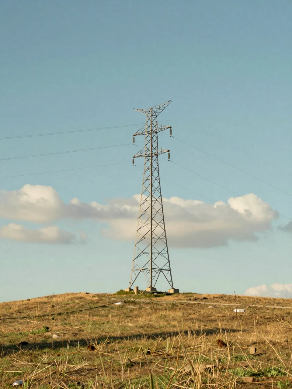 Transmission tower on a calm ridge in bright afternoon light with still grass.