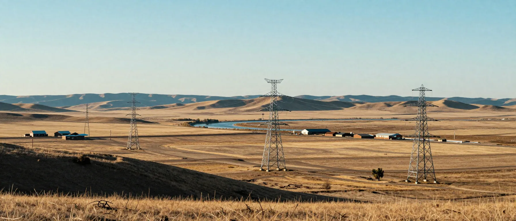Panoramic view of a transmission line crossing from foothills to prairie under a wide morning sky.