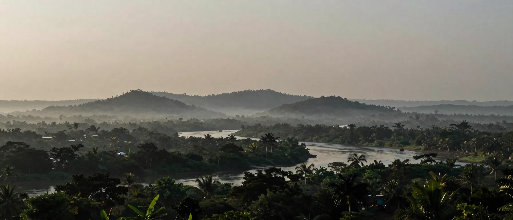 A wide view of forested hills and a river at dawn, with a band of pale smoke flattening the distant landscape.