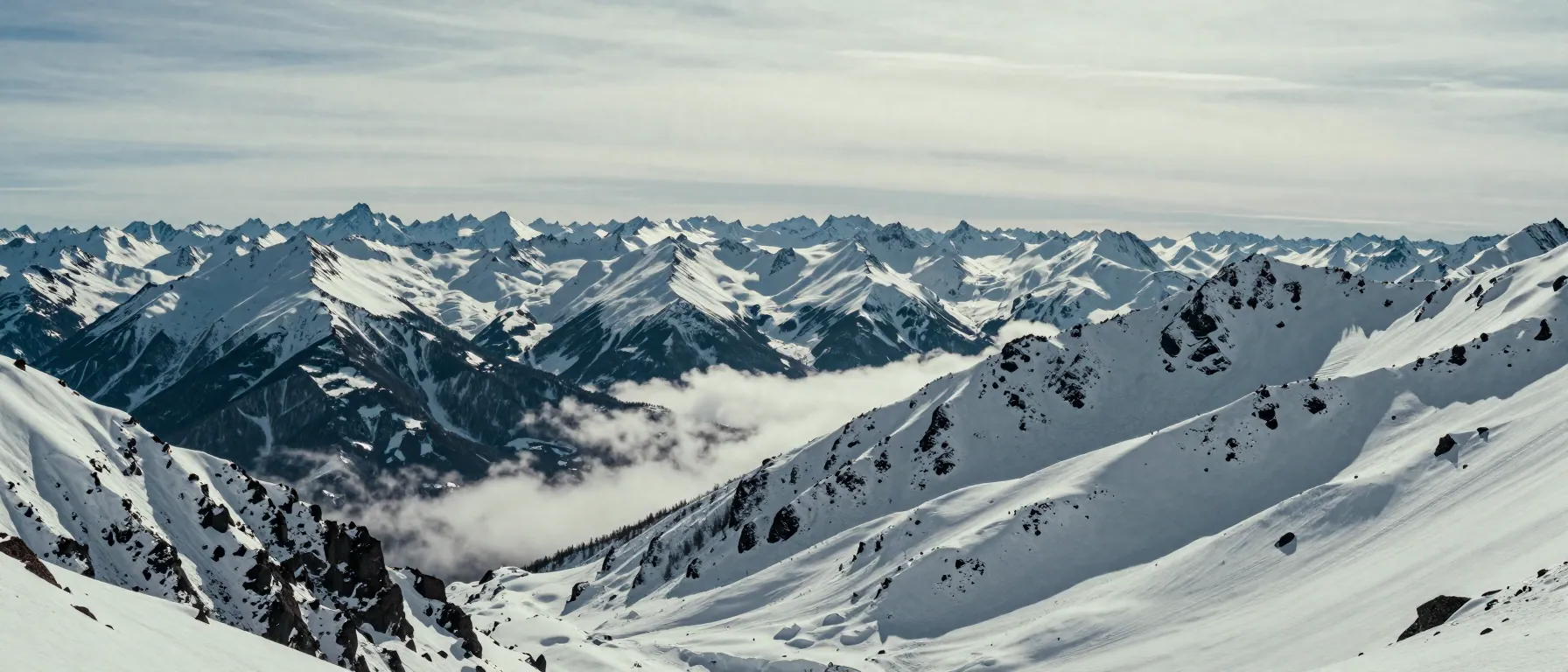 Panoramic winter mountain range with layered snowy ridgelines and low cloud in the saddles.