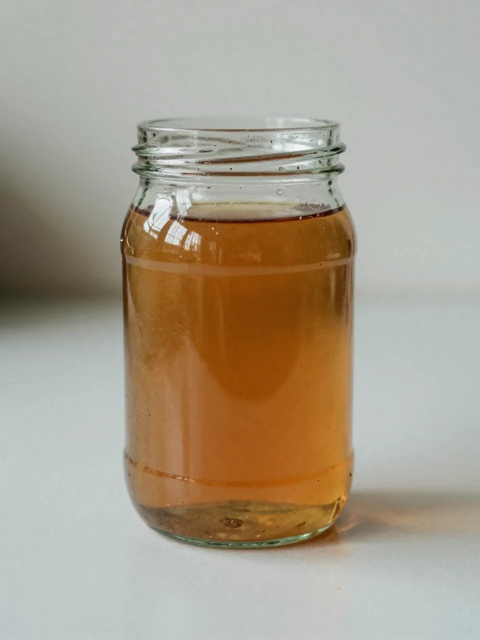 A glass jar of clean bright amber fuel on a workbench.