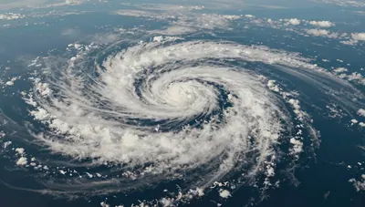 Aerial view of a spiralling tropical cyclone over open ocean, with thunderstorms curving around a low-pressure centre.