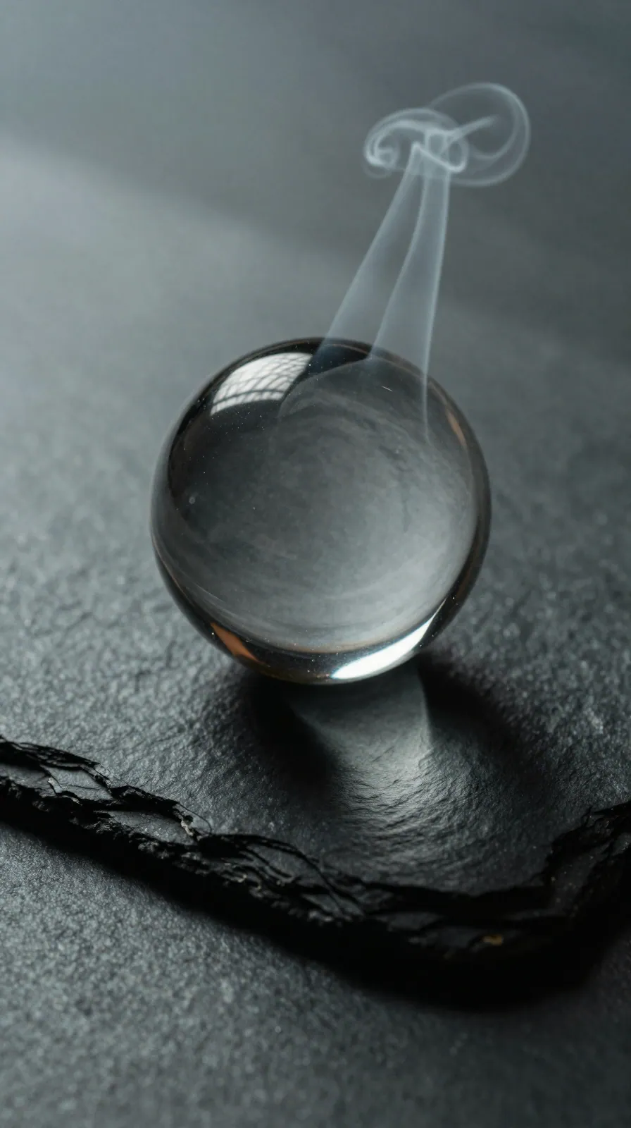 A glass sphere on dark slate reflecting blurred light, a thin curl of smoke behind it.