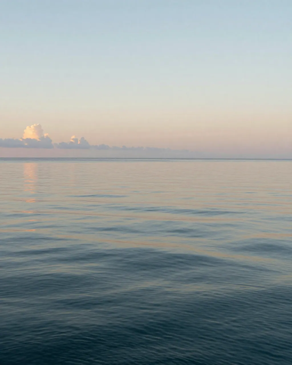 Calm tropical ocean at dusk with warm-toned surface water and distant low clouds.