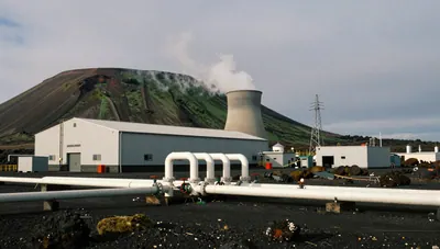 Geothermal power plant with steam pipes, turbine hall, cooling tower and transmission lines on a volcanic hillside