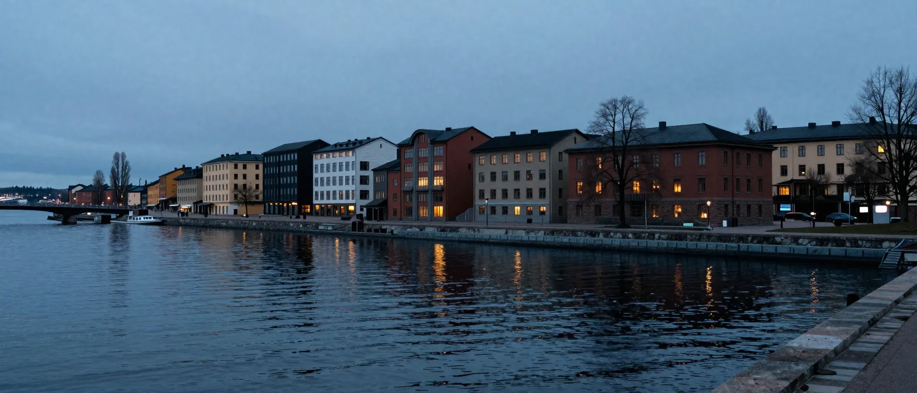 Wide blue-hour view of a Swedish waterfront with low buildings, a bridge and reflections on calm water.